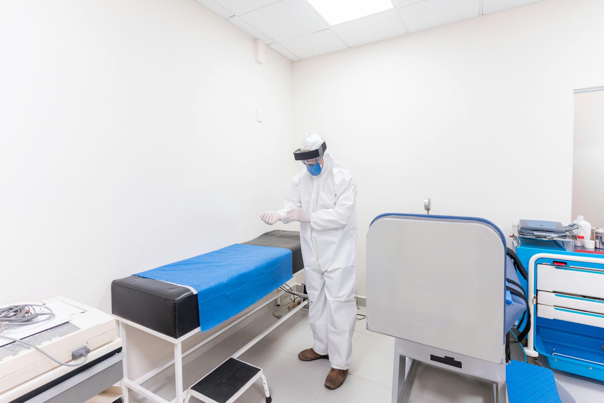 A healthcare worker in full PPE readies for work in a well-equipped hospital room.